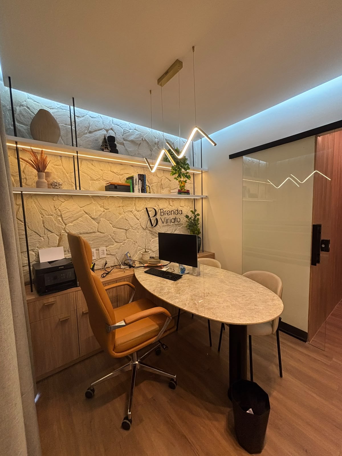 Sala de atendimento com mesa oval, estante iluminada e cadeiras para o cliente.
